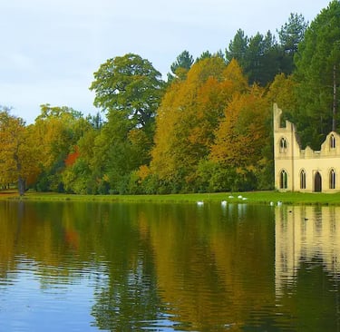 Autumn foliage and stone ruins reflecting in a calm lake at Painshill Park landscape garden.