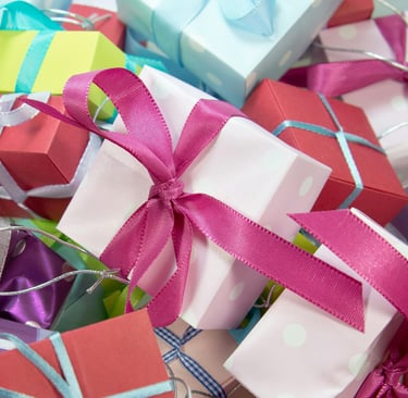 Pile of presents wrapped in paper with bows. In pink, purple, turquoise, yellow