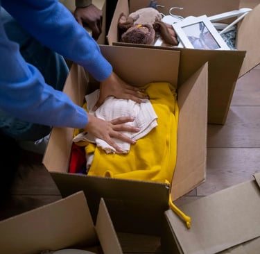A person packing yellow clothes into a cardboard moving box while relocating to a new home.
