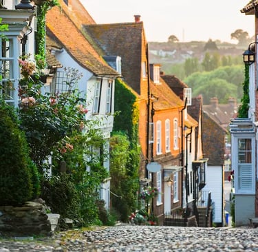 Quaint cobblestone street in Rye, England, with historic timber-framed houses and ivy at sunset.
