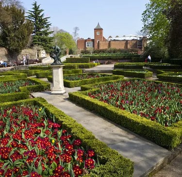 Formal English garden in Holland Park, red primrose flower beds, and a brick manor house in