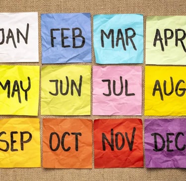 Twelve colorful sticky notes with months of the year arranged on a burlap background for calendar planning.