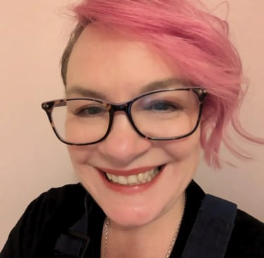 Jo de Serrano OBE, founder of Order from Chaos, smiling with bright pink hair, tortoiseshell glasses