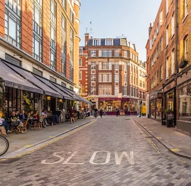 People dining at an outdoor sidewalk cafe on a cobblestone London street with brick buildings.