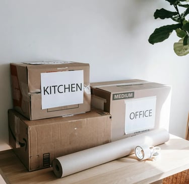 Cardboard moving boxes labeled Kitchen and Office on a table with packing paper and tape.