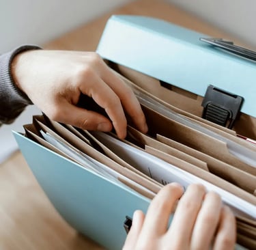 A person organizing business documents and paper files inside a light blue portable accordion folder.