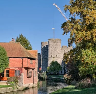 Historic Westgate Towers in Canterbury overlooking a river with autumn trees and a traditional brick house.