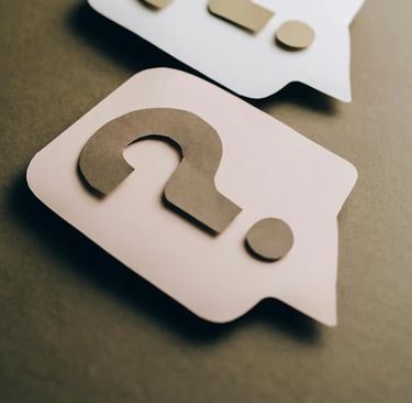 Two paper cutouts of question marks inside speech bubbles on a brown background representing help and FAQ.