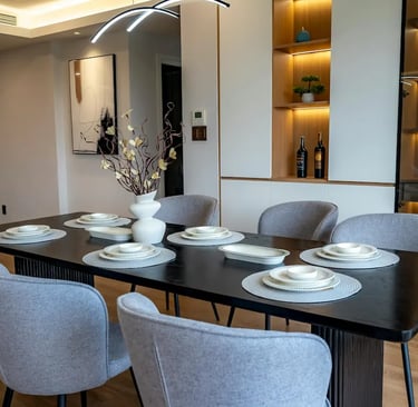 Modern dining room featuring a black table, gray upholstered chairs, and elegant table settings with minimalist decor.