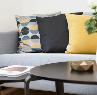 Modern grey sofa styled with yellow, black, and geometric pattern throw pillows near a coffee table.