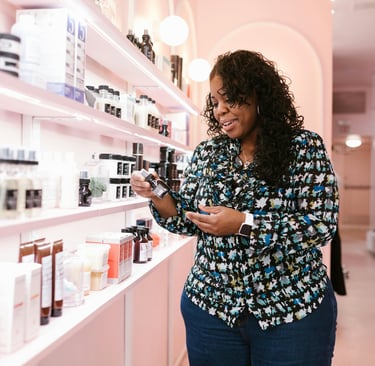 Mujer eligiendo producto en tienda de insumos de belleza con estante rosa lateral.