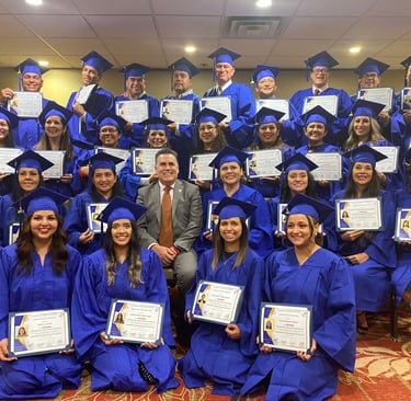 A diverse group of graduates in blue caps and gowns holding diplomas at a graduation ceremony.