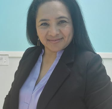 Professional portrait of a smiling woman in a black blazer and lavender shirt against a blue background.