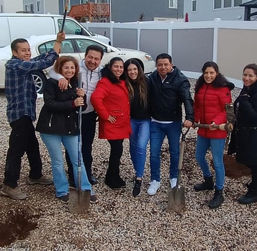 A group of smiling family members planting a new tree in their backyard with shovels.