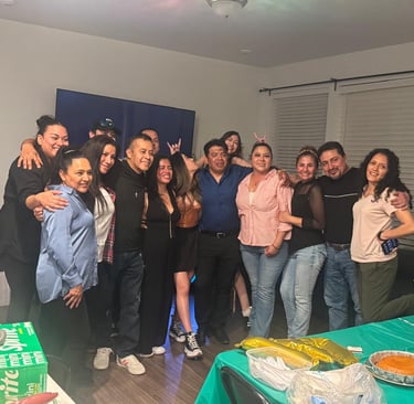 A large happy family celebrates a birthday party together in a living room with food and balloons.