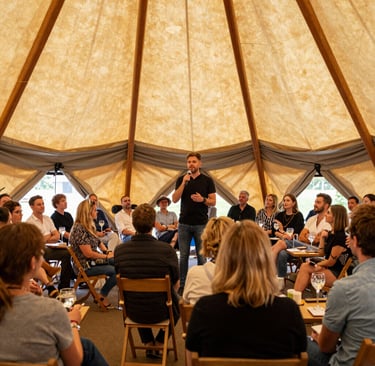 A speaker addresses a seated audience during a corporate retreat workshop inside a large canvas tipi tent.