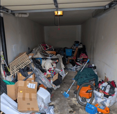 Deep Garage overfilled with a variety of items including pallets, outdoor toys, boxes, and furniture