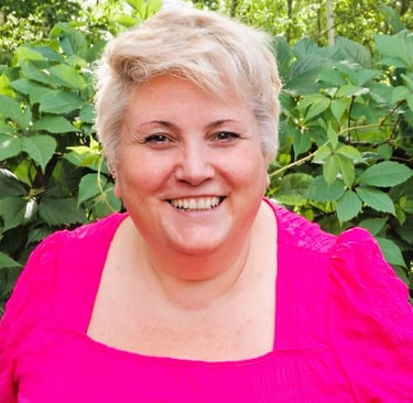 Naeratav lühikeste blondide juustega naine, kes kannab õues erkroosat toppi ja selja taga rohelisi l