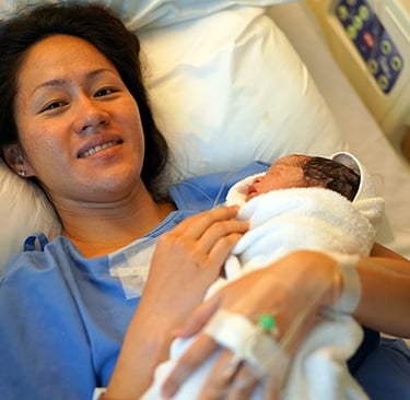 New mother lying in a hospital bed holding her newborn baby