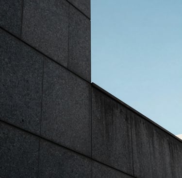 Detailed photography of a modern architectural detail in a Brazilian metropolis, featuring dark gray stone walls and a sharp corner reflecting a serene baby blue sky. The style is sophisticated, minimalist, and very clean.