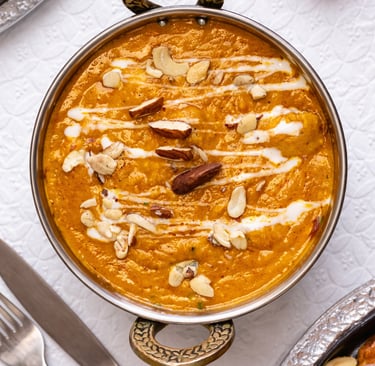 Creamy Indian butter chicken curry in a copper bowl garnished with cashews, almonds, and cream drizzle.