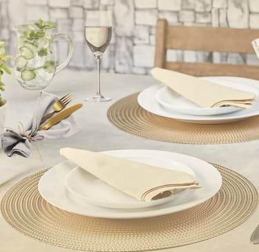 Mesa posta sofisticada em tons neutros com sousplat dourado, taças e guardanapos dobrados.