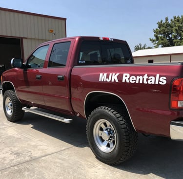 A team member from MJK Rentals securing a dumpster on the back of a flatbed truck, ready for transport.