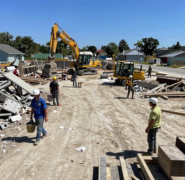 MJK Rentals’ truck hauling a heavy-duty dumpster down a suburban street lined with new home builds.