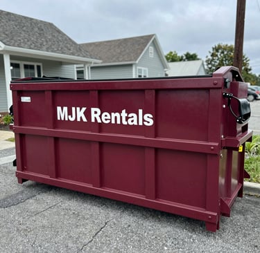 A large green dumpster filled with construction debris parked at a busy Manahawkin job site under a clear blue sky.