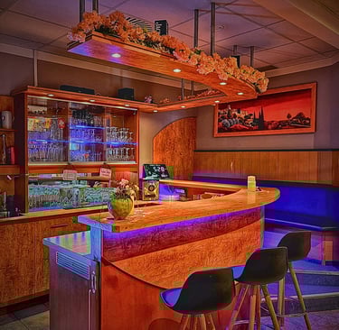 Modern wooden bar counter with colorful LED lighting, floral accents, and bar stools.