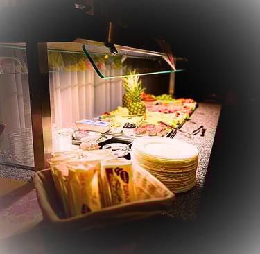 Hotel breakfast buffet featuring fresh pineapple, deli meats, cheese, and stacks of plates.