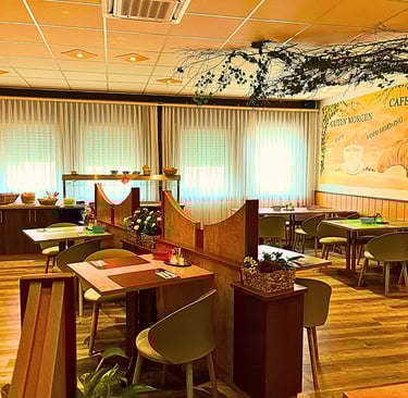 Cozy hotel breakfast room with wooden tables, cafe mural, and buffet area.