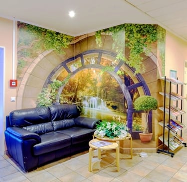 A waiting area with a black leather sofa and a nature wall mural featuring a waterfall and forest.