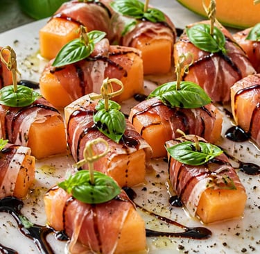 Prosciutto wrapped cantaloupe melon appetizers with balsamic glaze and fresh basil leaves on skewers.
