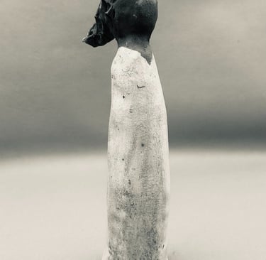 A handmade ceramic figurine of a slender woman in a long white dress, artfully crafted with dark clay details