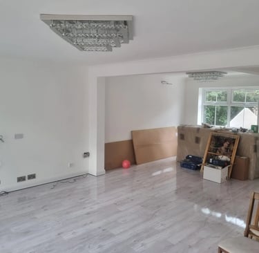 Modern living room with white walls, grey wood laminate flooring, and elegant crystal chandelier lighting.