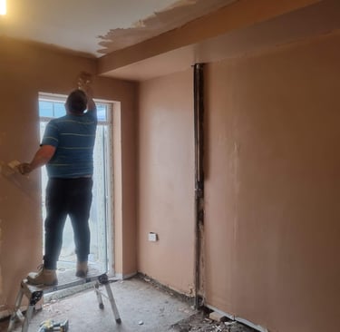Professional plasterer applying fresh plaster to a room ceiling and walls during a home renovation.