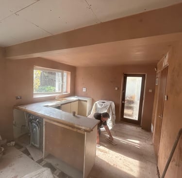 A professional plasterer applying finishing touches to fresh plaster walls in a kitchen renovation.