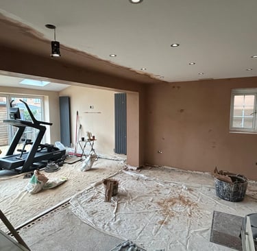 A room undergoing home renovation with freshly plastered walls and a treadmill on dust sheets.
