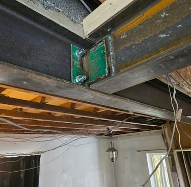 Structural steel I-beams joined by a green bolted splice plate during a home renovation.