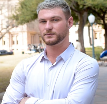 Professional portrait of a man with arms crossed in a white shirt at the Texas Capitol building.