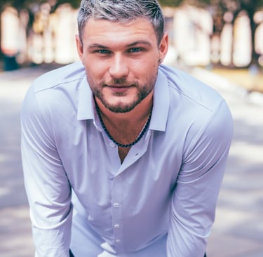 Young man with silver hair and a beard wearing a white button-down shirt outdoors.