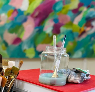 Painting tools and brushes on studio worktable with colorful painting in background