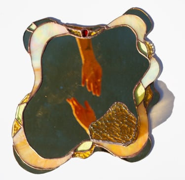 Espejo artesanal de vitral ondulado con borde iridiscente y el reflejo de unas manos extendiéndose
