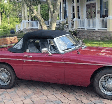 A sideview of a red MG MGB Roadster with black soft top.