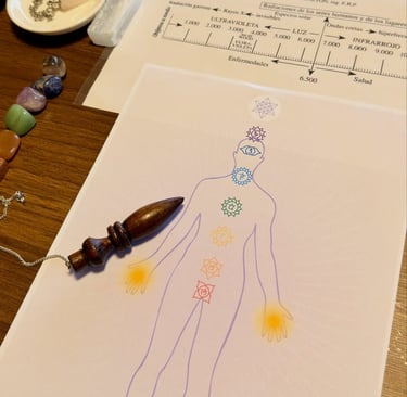Un péndulo de madera descansa sobre una tabla de sanación de chakras, cerca de un biómetro Bovis y v