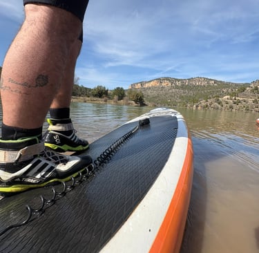 Primer plano de una persona sobre la tabla de paddle surf con grandes montañas al fondo