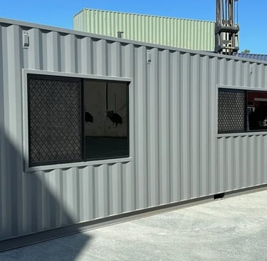 Modified grey shipping container office with installed glass windows and security screens.