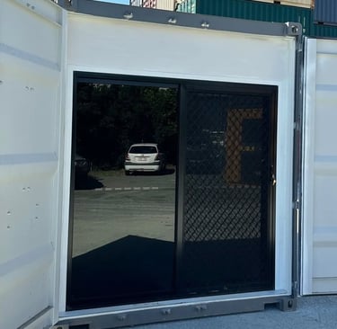 Modified shipping container with black sliding glass door and security screen mesh installed.