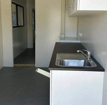 Compact modern kitchenette in a portable building featuring a stainless steel sink and dark countertop.